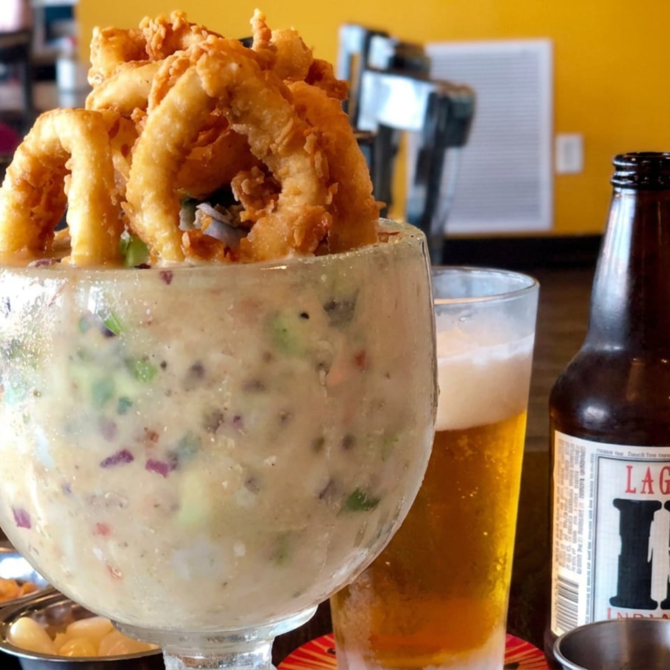Creamy seafood chowder topped with fried calamari rings, served beside a glass of beer and Lagunitas IPA bottle in a restaurant.