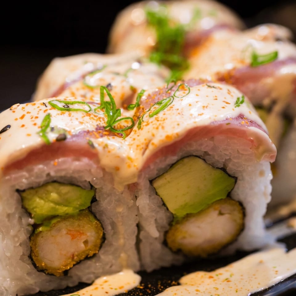Close-up of sushi rolls topped with salmon, creamy sauce, scallions, and spices on a black plate.