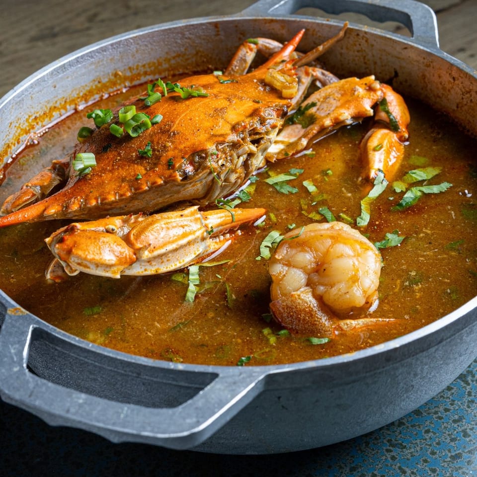 Whole crab and shrimp simmer in a richly seasoned sauce with chopped green onions and herbs in a large skillet.