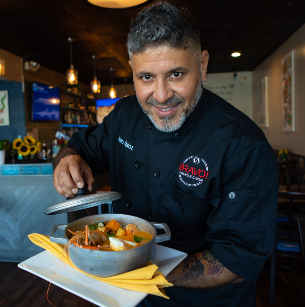 A portrait of Chef Beto Quiroz of Bravo Peruvian Kitchen holding one of his signature dishes.